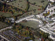 Aerial photograph of semicircular terrace of stone buildings with large expanse of grass in front and to the left. Also shows surrounding terraces of buildings.