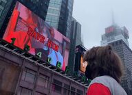 A photo of Ranboo looking at the billboard, containing a video of GL!Ranboo with red text saying "SAVE HIM"[28].