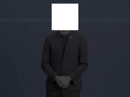 A person, with their face covered by a white box, in a suit wearing a Showfall Media lapel pin.