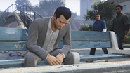 Michael sitting on a bench. Franklin and Lamar are seen in the background.