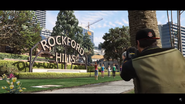 Beverly Felton taking a photograph of women practicing yoga outside the Rockford Hills Sign from behind a tree.