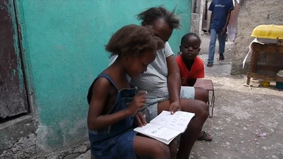 A young girl practices reading with her grandmother on a quiet afternoon in Bicentennaire, turning a narrow passageway into a study hall.