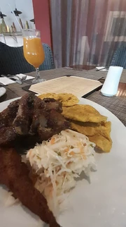 A classic Haitian combo of seasoned meat, fried plantains, akra, and pikliz, with a fresh juice on the side.