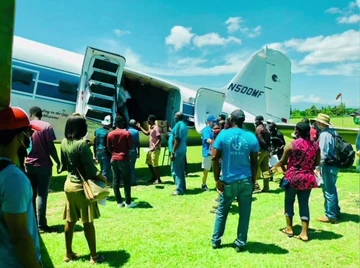 Passengers and aid workers board a Missionary Flights International aircraft on the grass apron at Pignon Airport.