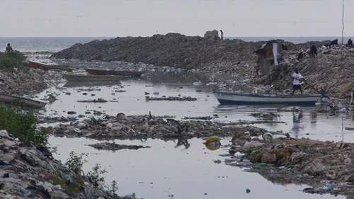 Cité l’Éternel shoreline. Every bottle tells a story — of someone upstream. Most of this trash started its trip in other parts of Port-au-Prince. By the time it reaches Bicentennaire, it has already passed through several neighborhoods, collecting not just debris — it carries the city’s habits.