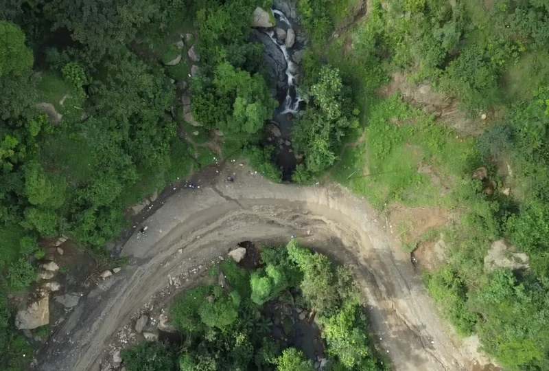 Aerial view of a sharp bend along RN-3 in Grand-Gilles, where a seasonal stream crosses the roadway—demonstrating how runoff and inadequate drainage directly impact road safety and circulation.