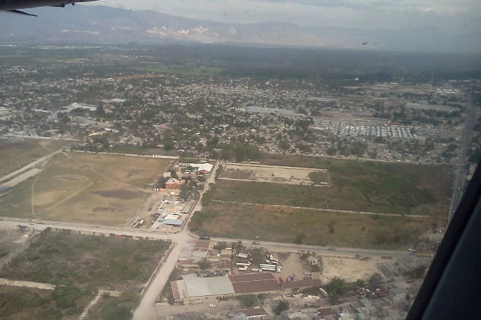 Aerial view of the coastal plain west of La Saline, with open lots near Fort Dimanche in the foreground and the wider urban area extending toward Cité Soleil in the distance.