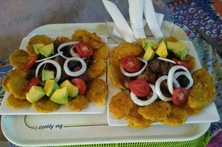 A classic Haitian platter of griot and bannann peze, topped with avocado, tomatoes, and fresh onions - Served at Vanise.