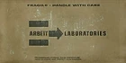 The Arbeit Laboratories logo on a cardboard crate texture.