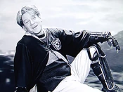 Lockhart sur un balai, portant une robe aux couleurs de .