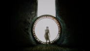 Senua observing the large portal with nordic runes located at the end of the vast corridor
