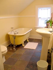 an upstairs bathroom with toilet, claw foot tub, sink, window, tile floor and slanting upper wall