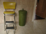 a "retro" step stool, a metal framed, high seated chair with retractable steps, tile floor and wall, trash can