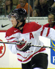 A hockey player in white and red uniform speed-skates across the ice, stick held at chest level.