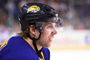 A closeup of an ice hockey player focusing on his head and shoulders. He is looking to the right and is wearing a black helmet and a blue uniform.