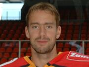 An ice hockey players face and shoulders. He has short blrown hair and is not wearing a helmet.