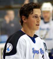 Head and shoulders of a hockey player in white and blue uniform, without his helmet on