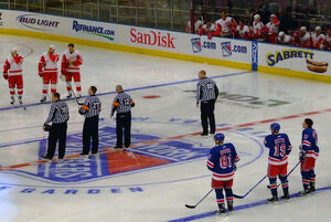 Officials, from left to right: Michel Cormier (linesman), Eric Furlatt (referee),  (referee), and Scott Driscoll (linesman) stand at centre ice for the national anthem before a game in  between the  and .