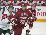 A group of three ice hockey players skate to the right of the image while looking to the left. The image is focused on the middle player, who is wearing the same uniform of the skater to his right, who is partially concealed by his teammate