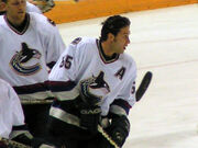 A hockey in white uniform without his helmet on looks to the right of the camera.