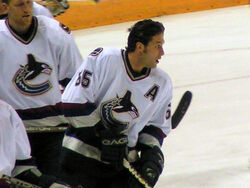 A Caucasian hockey players skates on the ice without his helmet in a relaxed fashion. He is looking to the right and is dressed in a white jersey with blue and maroon trim.