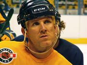 A headshot of an ice hockey player on the ice. He is wearing a yellow jersey and a black helmet.