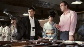 Tiger Tanaka (Tetsuro Tamba) demonstrating the pistol Gyrojet to James Bond and Aki.