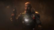 Man sieht Saw Gerrera in einem Kampfanzug, ähnlich einer Rüstung. In der rechten Hand hält er einen Blaster, der nach oben zeigt. Sein Mund ist schief, er trägt Bart und hat eine Glatze. Der Hintergrund ist verschwommen.