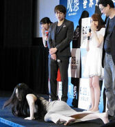 Saisho frightens the cast and director as Kayako at the press release.