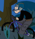 In Mission Outfit with safety helmet, goggles and microphone as he stubbornly cycles up to the mission location, separate from Kim.