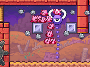 A purple Clanksprout smashes metal blocks in order to grab a Kirby.