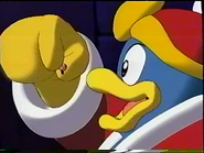 A shrunken Kirby held in Dedede's fingertips.