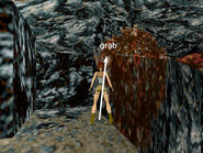 Turn left, so the lava pool is on Lara's right and walk forward until Lara touches the wall. Take one hop back, then sidestep as far as possible to the right so Lara's right foot is at the edge of the pit. Now turn about 10 degrees to the right so Lara is facing the wall just above and to the right of the edge, as shown in the screenshot above. Take a standing jump to grab the horizontal seam in the wall.