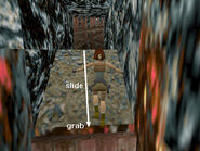 Turn around to face the wooden door. Slide down the slope and grab the edge as the trapdoor opens beneath Lara.