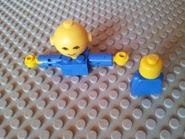 To the left is the head, arms, and upper torso of a Homemaker figure; to the right is the head and torso of a LEGOLAND minifigure
