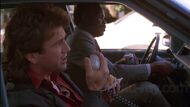 Murtaugh in his detective squad car with Riggs responding to dispatch.