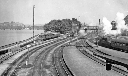 Über das Gleisvorfeld des Bahnhofs hin zum Bahndamm hier eine historische Aufnahme von 1958, links zu sehen: die Auffahrt zur alten (hier durch die Signalbrücke und Dampfwolken verdeckte) Brücke