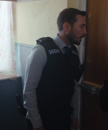 Arnott with stab vest and firearm during a raid of Pulton House (Series 5).