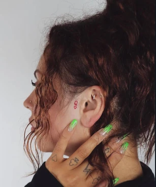 Queen of hearts on Jesy's left side of her face and the card suits on her left fingers