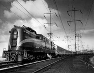 A GG1 is pulling several burgundy passenger cars.