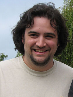 Causcasian man with medium-length dark brown hair and a beard smiles for a camera