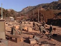 A view of the devastation caused by the storm. The point of view is looking to the southeast from just behind the latrine (which can just be seen to the extreme left). The officers club is the metal shed in the center left. The camouflage net covers the accomodation tents. The hill in the background center is where Klinger is standing.