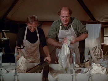 The interior of the laundry tent as seen in . It has a couple of large sinks made from barrels, much like in the scrub room. There are wash boards, and hanging on the wall can be seen various wash basins.