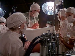 Hawkeye calls to "Amanda" to bring adrenaline. This is the best view of her. She is the one on the extreme right inserting the adrenaline into the IV. The anaesthetist in the foreground is Margaret.