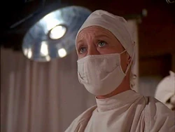 This unnamed and uncredited nurse in a demanding surgical scene has some lines and looks older than the other extras who play nurses. She is also given quite an extensive close up shot. It is speculated that she might be Connie Izay.