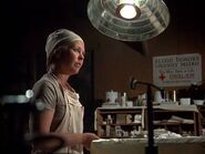 Scene from Season 9 "No Sweat". Earlier she was assisting Hawkeye in the O.R. and addressed by name. Here she is tidying up after the op. She is astonished to hear Margaret and Potter talk about her prickly heat condition being broadcast over the P.A. by mistake.