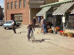 Opie bicycles in front of the market. The theater is missing its front behind him.