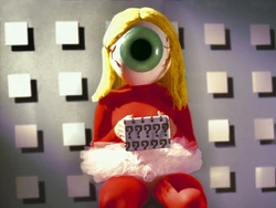 Frame of "The Act of Being Polite" showing a woman with an eyeball mask holding a box.