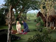 A man and a woman sit at a picnic blanket, surrounded by nature, with a futuristic city in the distance