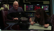 Picard operates the armrest intercom while Troi grips her console handrail in 2379